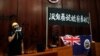 一名进入香港立法会的抗议者站在挂在立法会内的港英旗帜旁使用扩音喇叭讲话。（2019年7月1日）